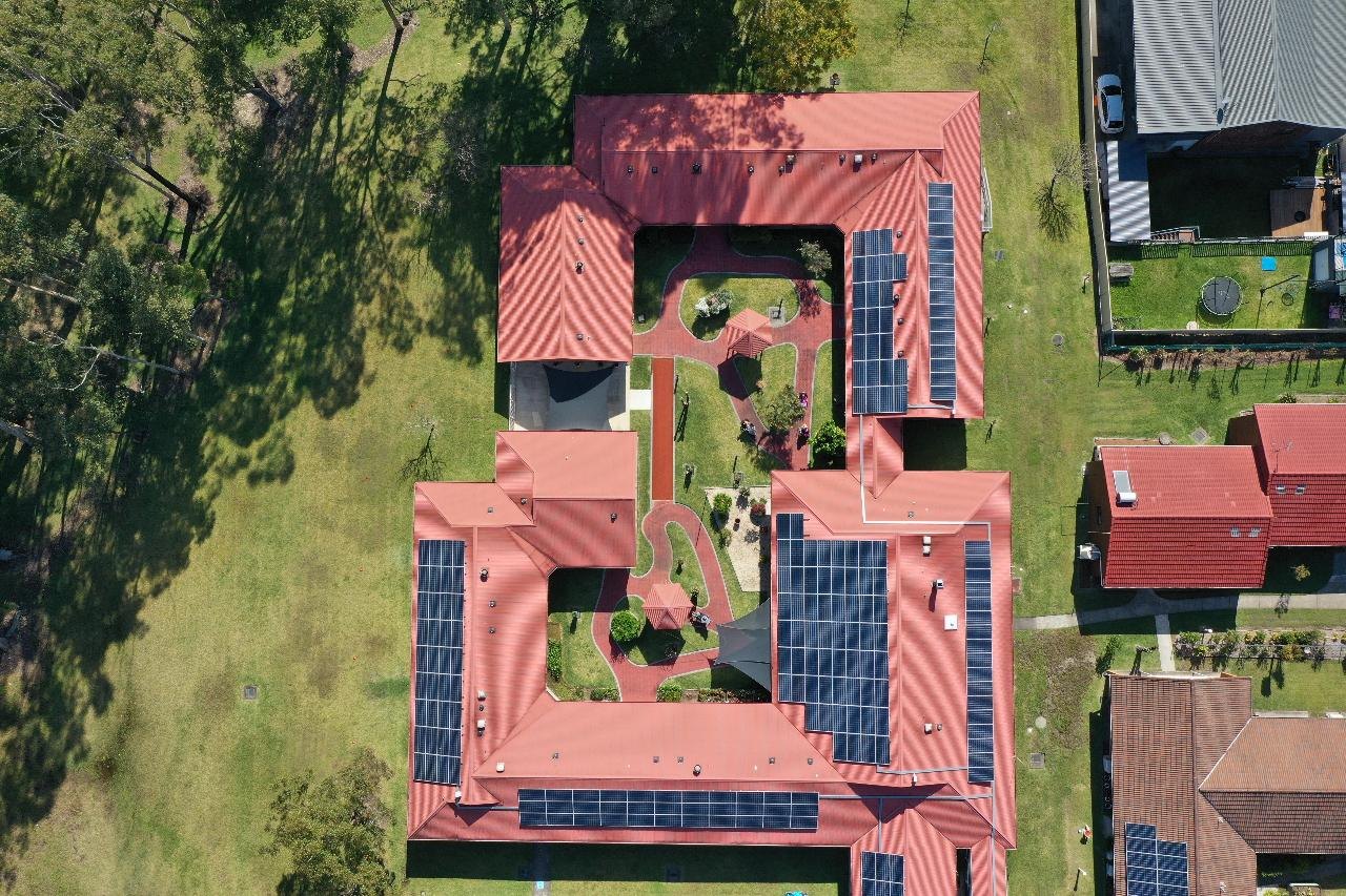 Overhead aerial photograph of a property with a red roof, surrounding trees and solar panels